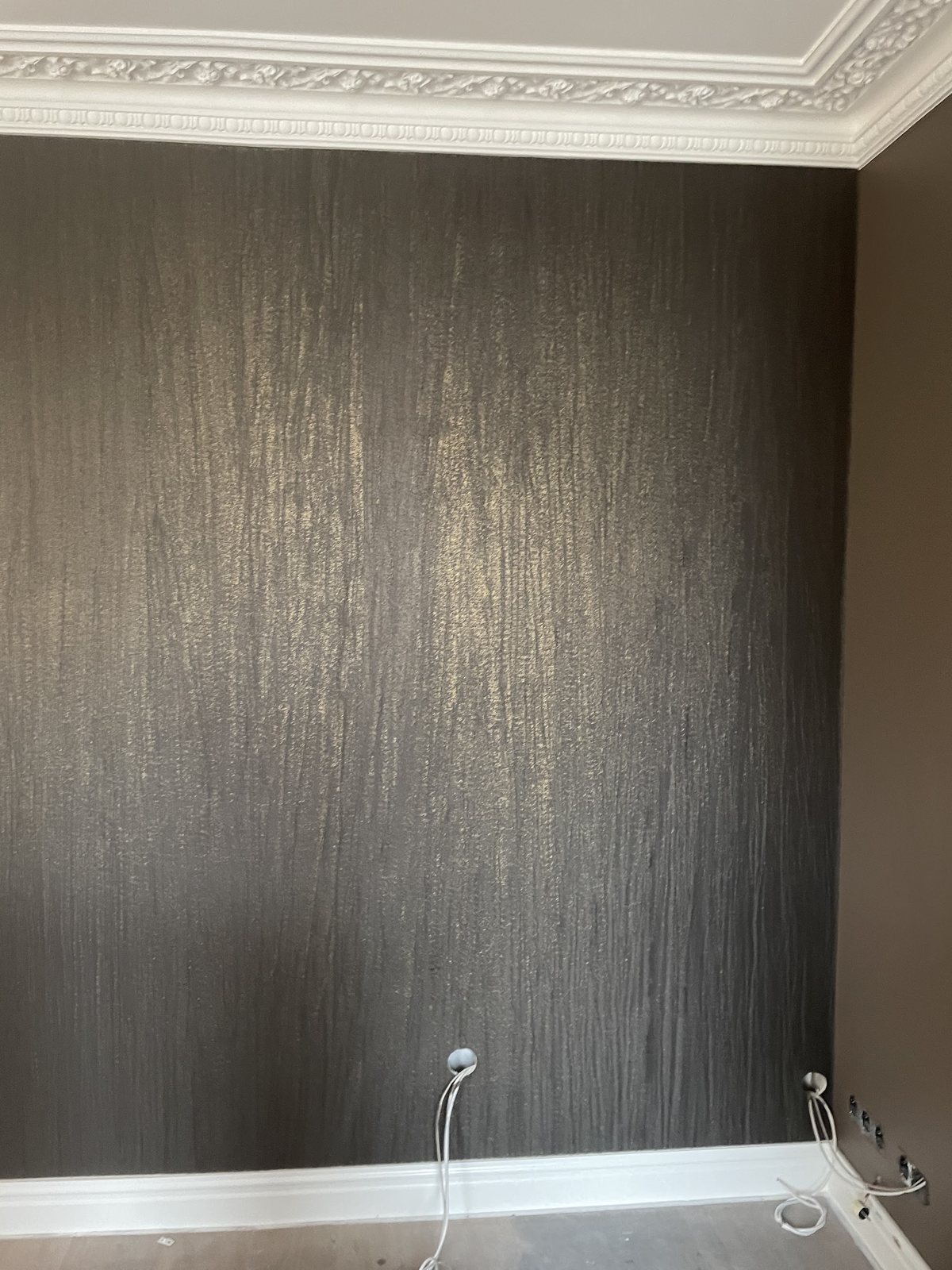 Donkere bronskleurige behangwand met structuur onder een witte siercornice