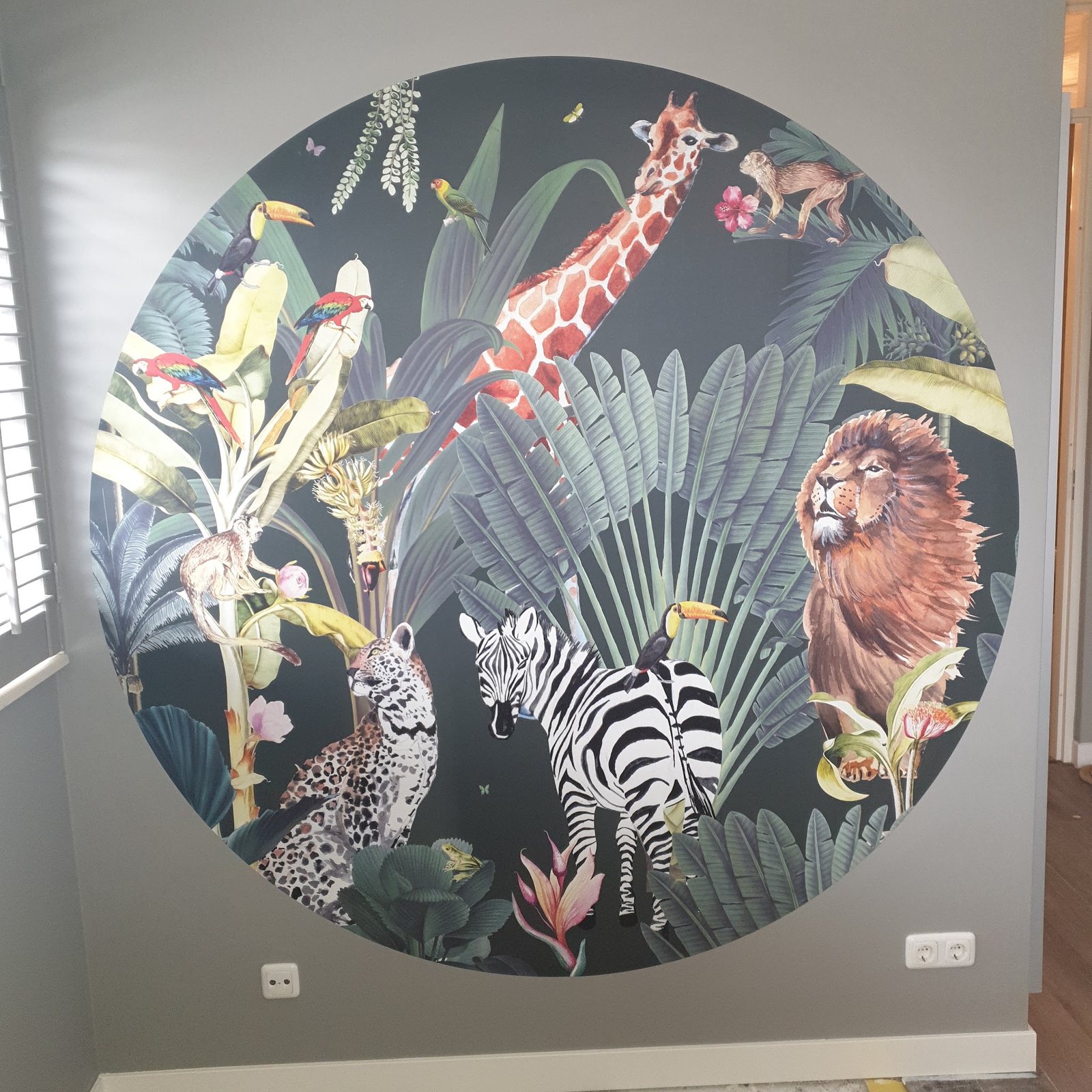 Ronde fotowand met een giraffe, leeuw, zebra en luipaard tussen jungleplanten op een grijze muur
