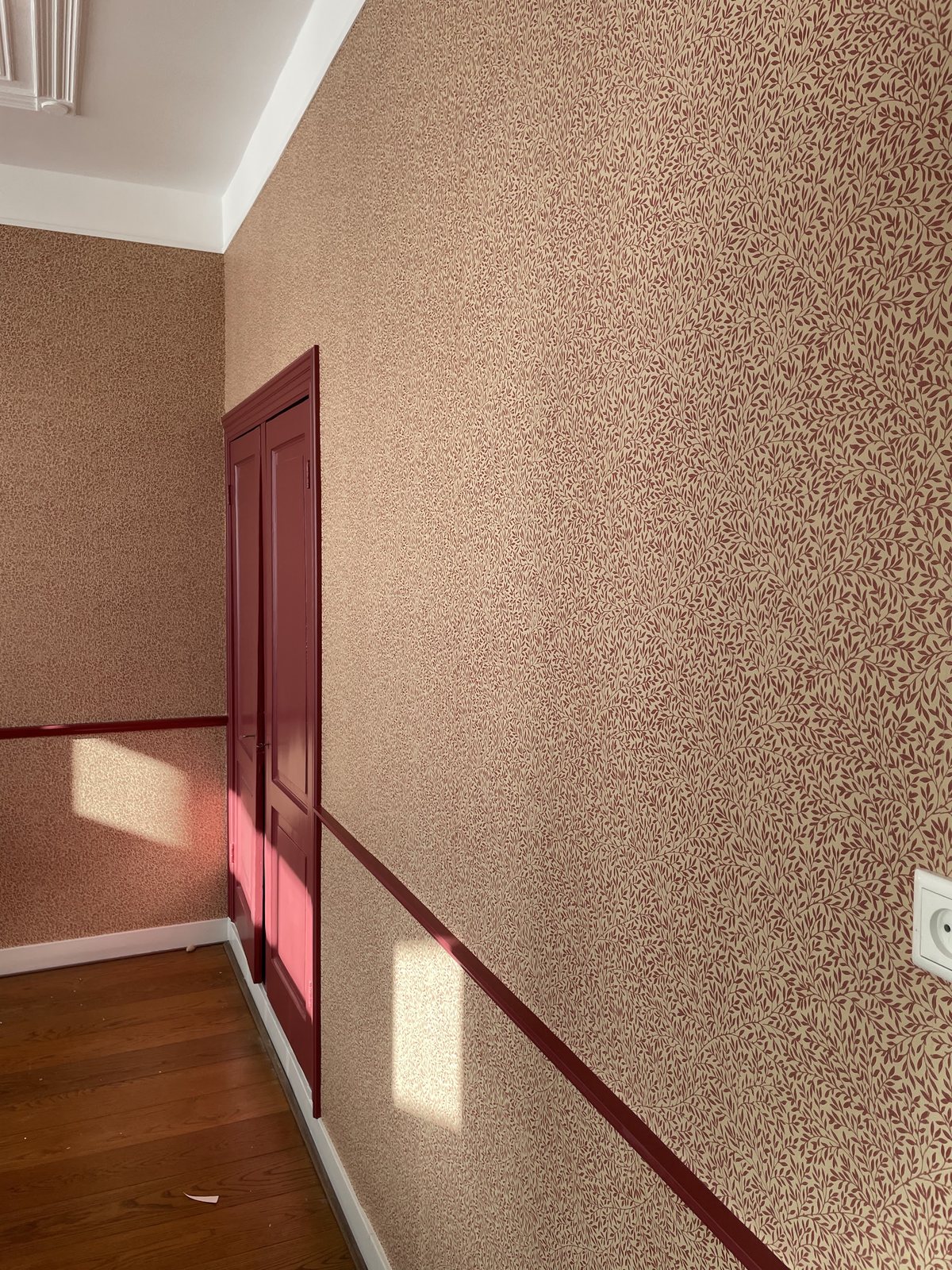 Gang met gespikkeld terracotta behang en een diep rood geschilderd deurkozijn met lambrisering