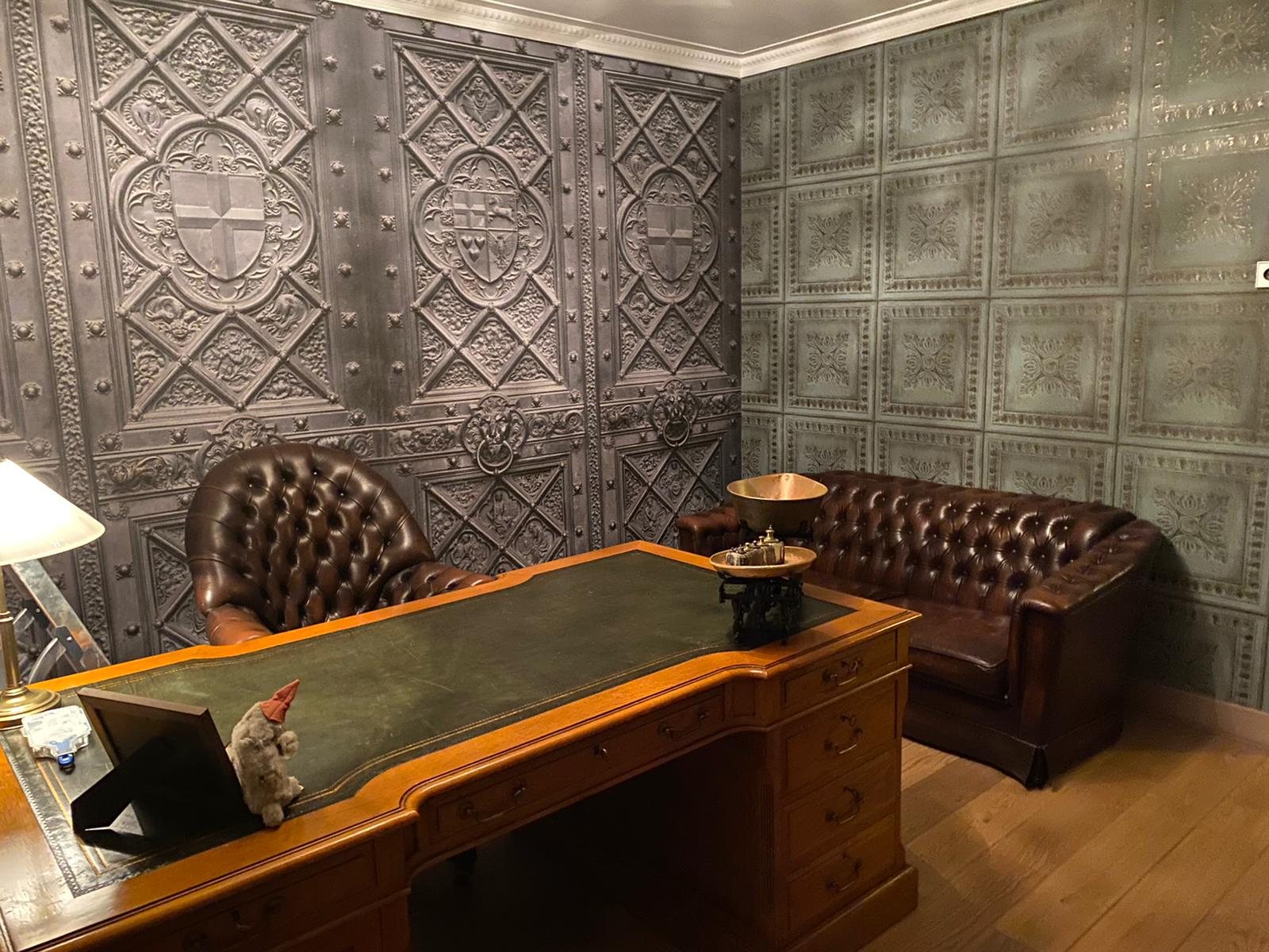 Werkkamer met behang in de look van geperst metaal, een chesterfield bank en een antiek bureau